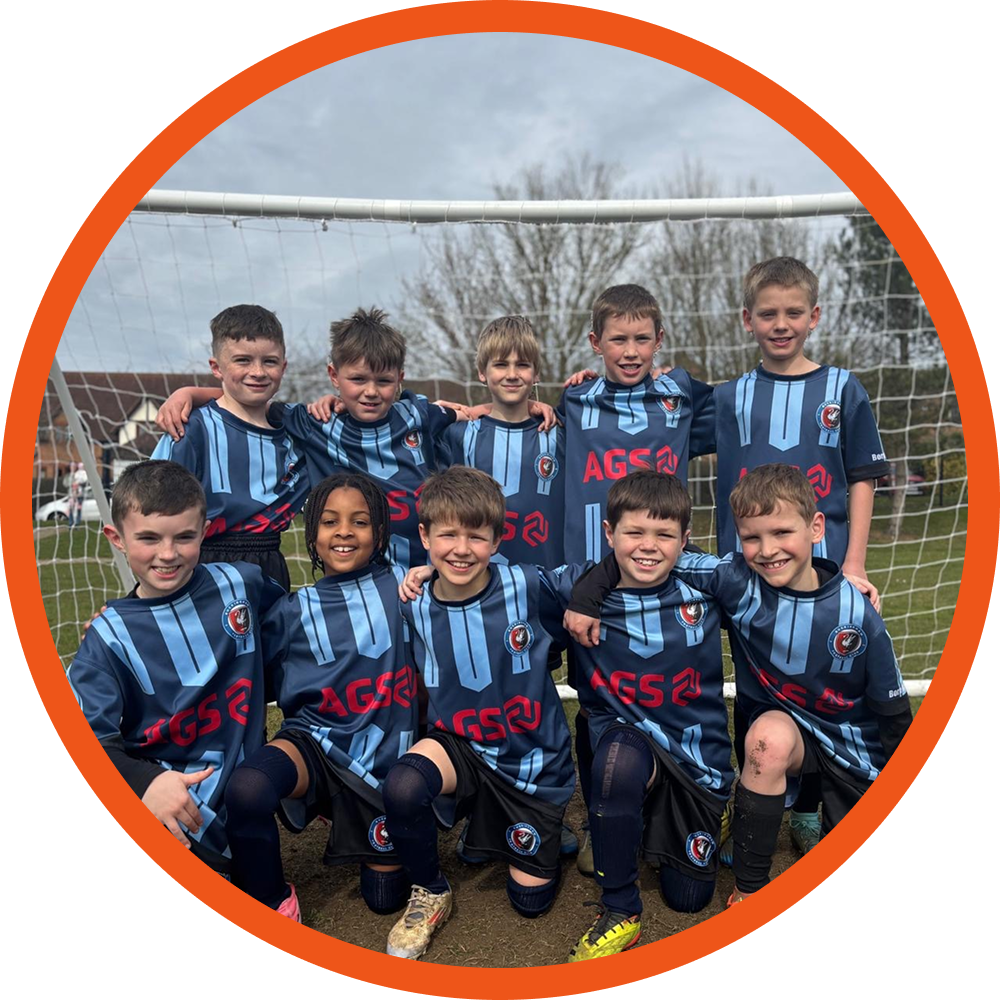 Boys in football kit smiling standing in front of a goal on the pitch